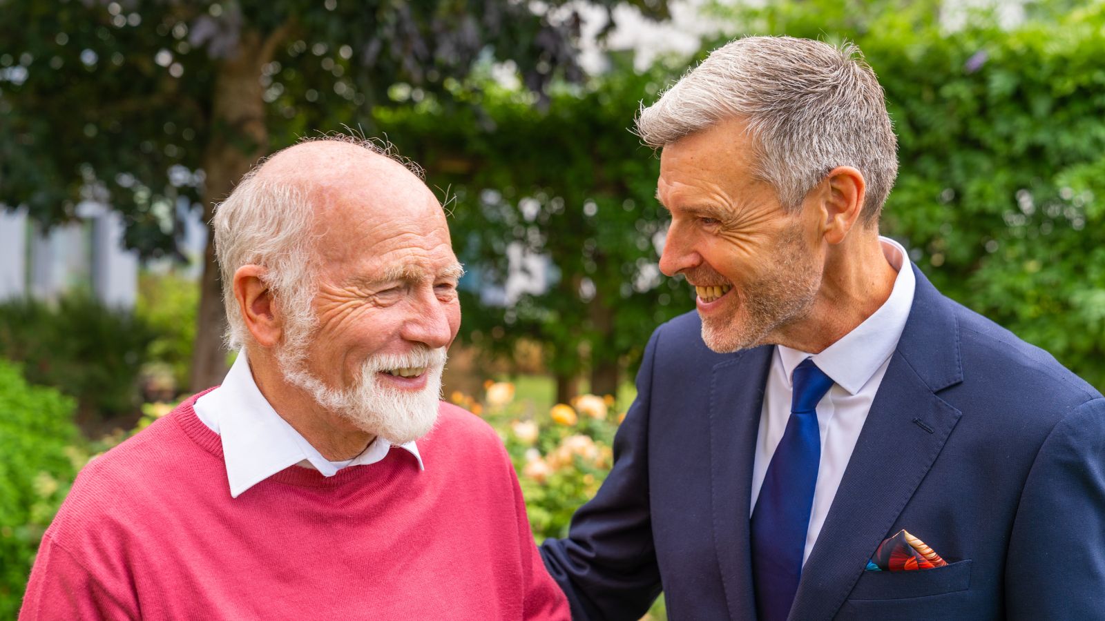 A resident and a member of staff standing together in the garden and laughing