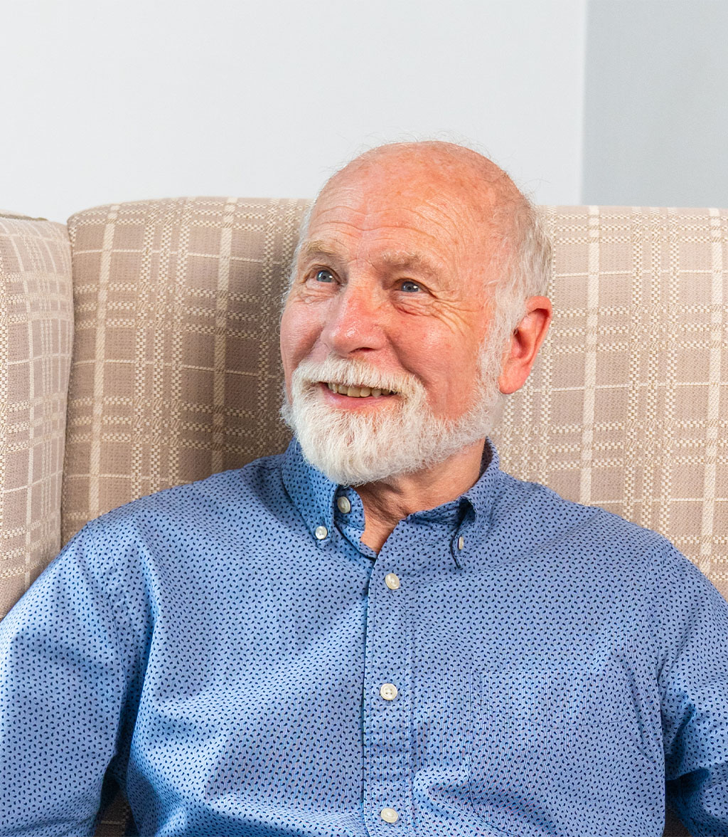 Older gentleman smiles off camera seated in an armchair